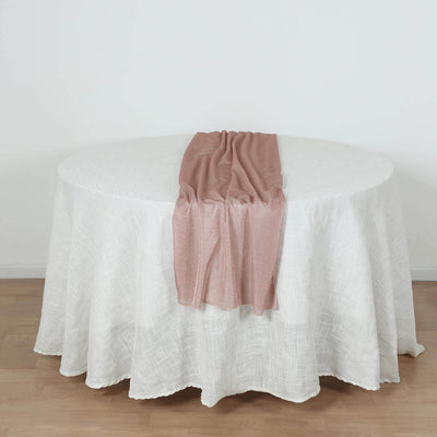 Round table with a white tablecloth and a rose gold runner draped on top.