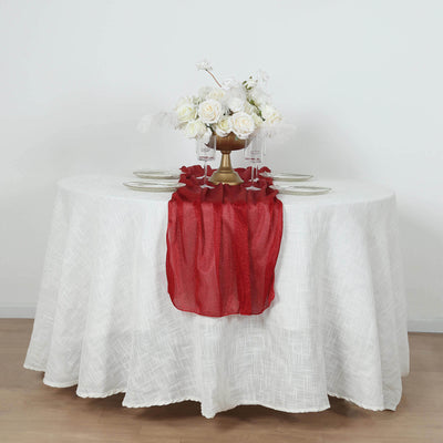 Red table runner on a white table with floral centerpiece and dinnerware.