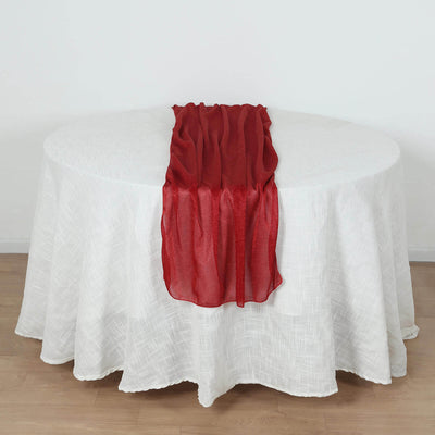 Red sheer table runner on a white tablecloth in a studio setting.