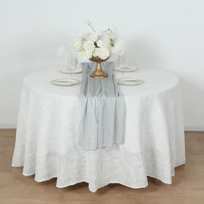 Elegant round table set with white tablecloth, silver runner, and floral centerpiece.