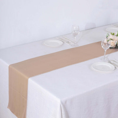 Beige satin table runner on a white dining table with plates and glasses.