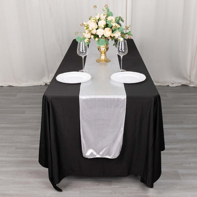 Elegant black table setting with silver runner, plates, and floral centerpiece.