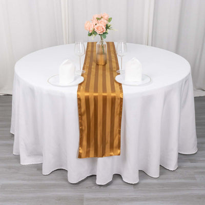 Elegant round table set with a gold striped runner, flowers, and glassware.