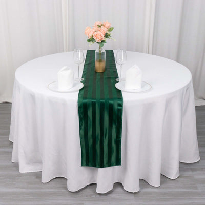 Green satin table runner on a round table with white tablecloth and floral centerpiece.