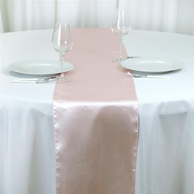 Pink satin table runner on a white table setting with plates and glasses.