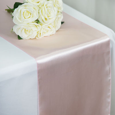 Pink satin table runner with white roses on a white table.