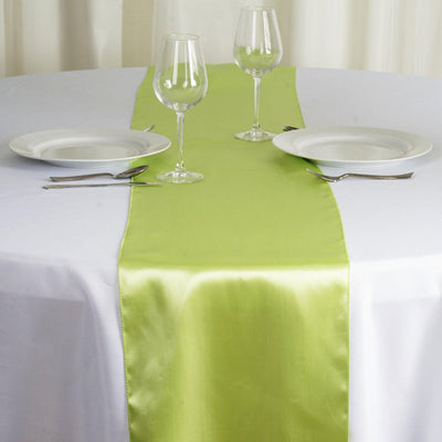 Green satin table runner on a white table with plates and glassware.