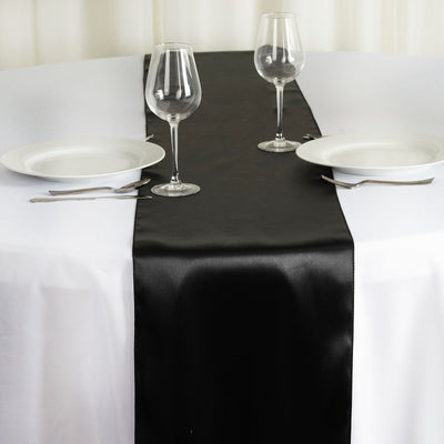 Black satin table runner on a white table with plates and glasses.