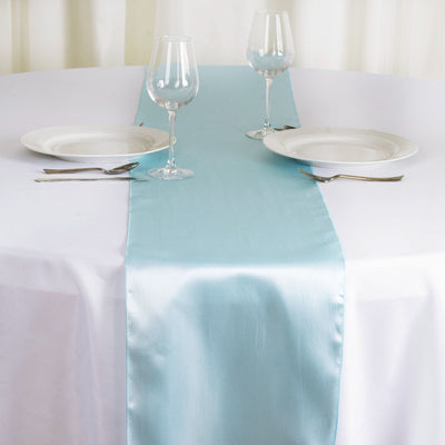 Light blue satin table runner on a white table setting with glassware and plates.