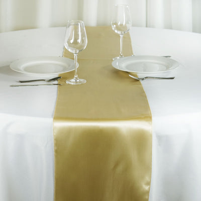 Gold satin table runner on a white table with plates and glasses.