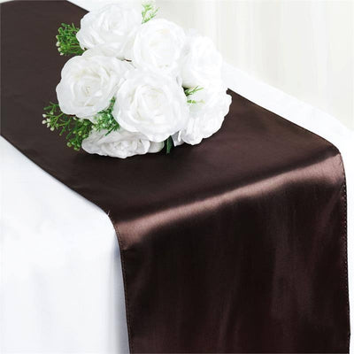 Brown satin table runner with white floral arrangement on top.