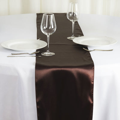 Brown satin table runner on a white table with plates and glasses.