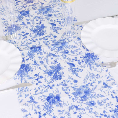 Blue floral table runner on a white table setting with plates and cutlery.