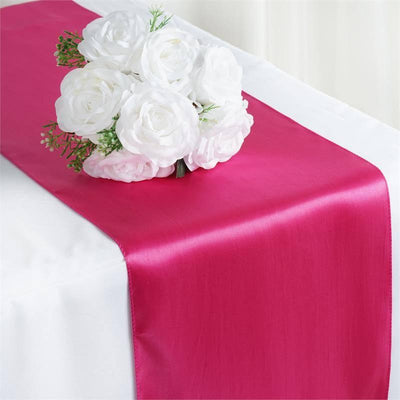 Pink satin table runner with white floral bouquet centerpiece.