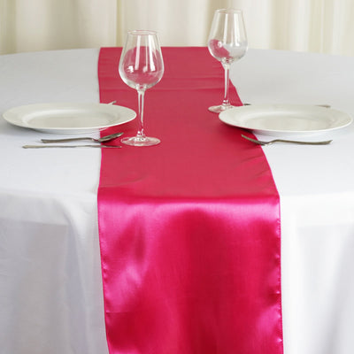 Hot pink satin table runner on a white table setting with plates and glasses.