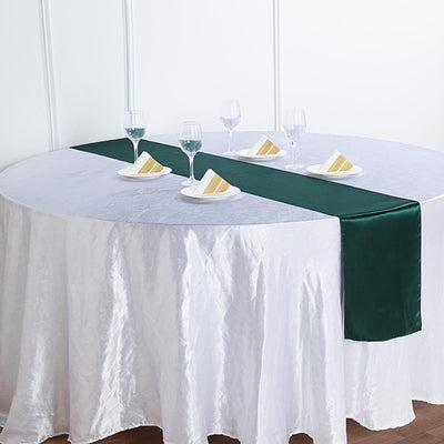 Green satin table runner on a round dining table set with plates and glasses.