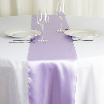 Purple satin table runner on a white table with plates and glasses.