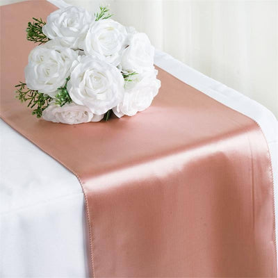 Rose gold satin table runner with white faux roses arrangement on top.
