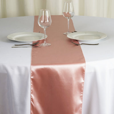 Pink satin table runner on a white table with plates and glasses.