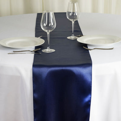 Navy satin table runner on a white table with wine glasses and plates