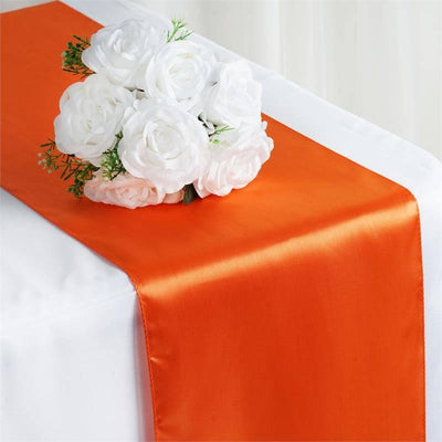 Orange satin table runner with white floral arrangement on a table.