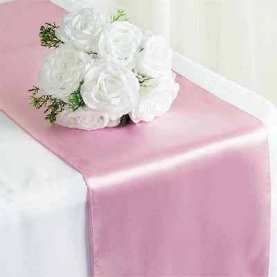 Pink satin table runner with white rose bouquet on a table.