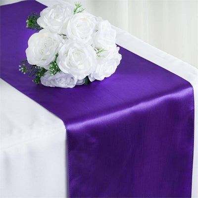 Purple satin table runner with white flower bouquet on a white table.