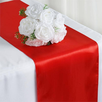 Red satin table runner with white floral arrangement on a table.