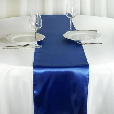 Blue satin table runner on a white table with plates and glasses.