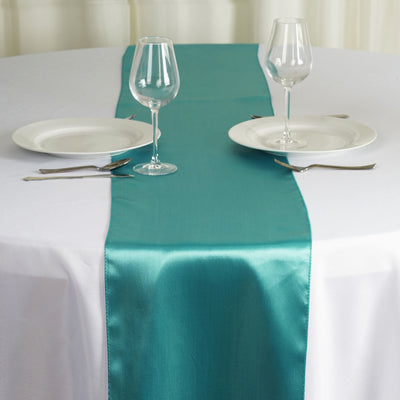 Teal satin table runner on a round dining table with plates and glasses.