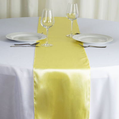 Yellow satin table runner on a white table with plates and glasses.
