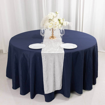 Elegant round table setup with navy tablecloth, white runner, and floral centerpiece.