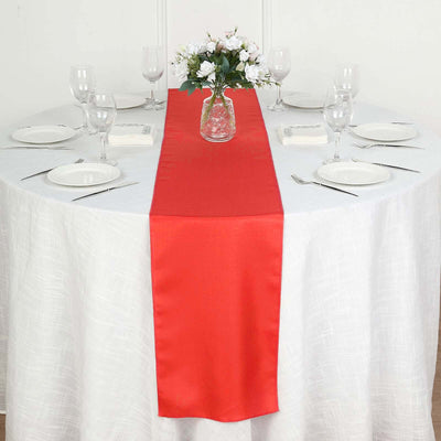 Red table runner on a white table setting with floral centerpiece.