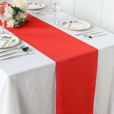 Red table runner on a white table setting with elegant plates and glassware.