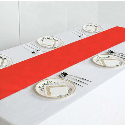 Red table runner on a white table with plates and cutlery arranged.