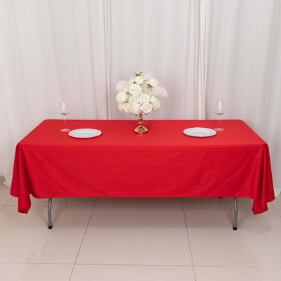 Red tablecloth with plates and a floral centerpiece on a dining table.