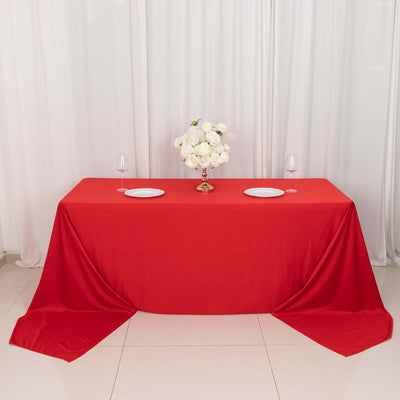 Red tablecloth with white plates and floral centerpiece on a dining table.