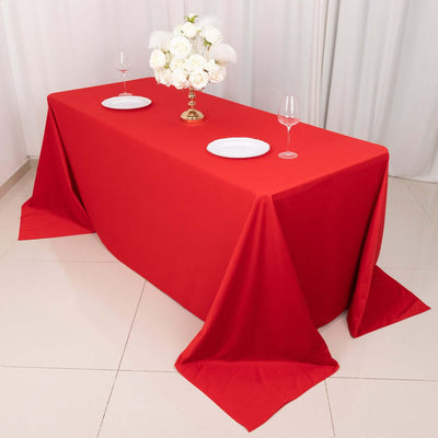 Red tablecloth on a dining table set with white plates and floral centerpiece.
