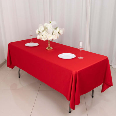 Red tablecloth set with white plates and a floral centerpiece.