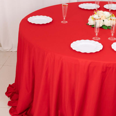 Red tablecloth draped over a round table with white plates and floral centerpiece.