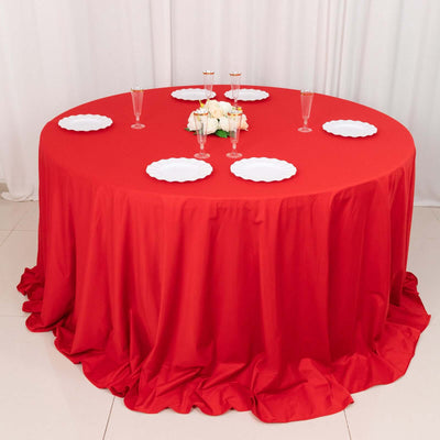 Round red tablecloth with white plates and floral centerpiece for elegant dining.