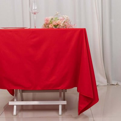 Red tablecloth draping over a table with a floral arrangement and wine glass.