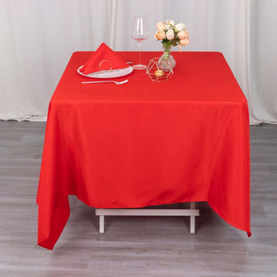 Red tablecloth on a dining table with glassware and floral centerpiece.