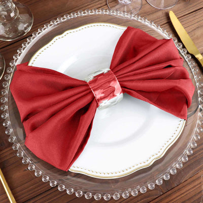 Red fabric napkin elegantly tied on a white plate with a silver napkin ring.