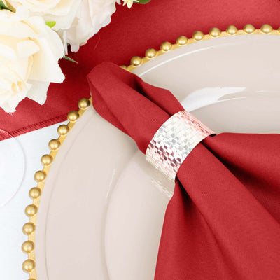 Red napkin elegantly styled with a hammered silver napkin ring on a decorative plate.