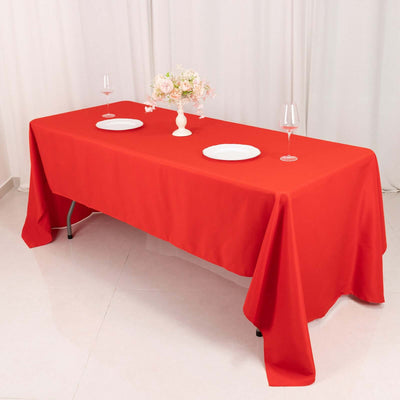 Red tablecloth draped over a dining table with plates and floral centerpiece.