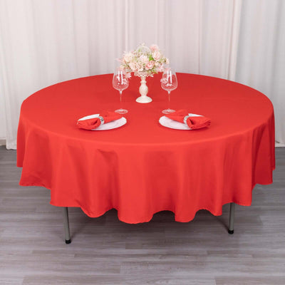Red round tablecloth elegantly set for a dining scene with floral centerpiece and tableware.