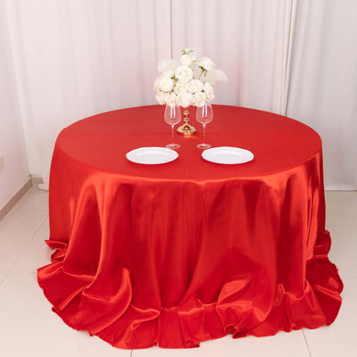 Elegant round table set with red satin tablecloth, white plates, and floral centerpiece.