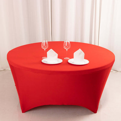 Red round tablecloth with plates and glasses set for dining.