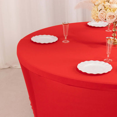 Red tablecloth draping a round table with white plates and elegant glassware.